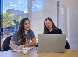 Duas funcionárias olhando o celular na área de convivência da empresa