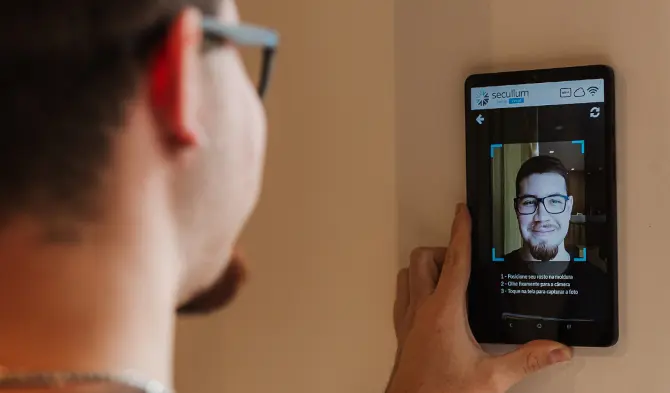 Homem olhando para um tablet, que está fazendo o reconhecimento facial no aplicativo do Acesso Controlador
