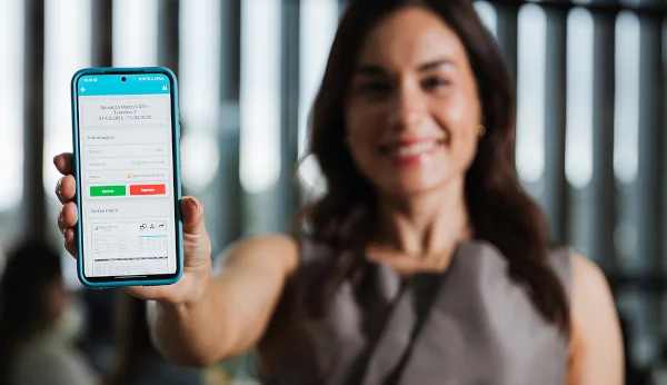 Mulher sorrindo segurando um celular com a tela do app central do funcionário